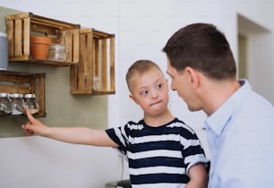 A father with happy down syndrome son indoors in kitchen, cooking.