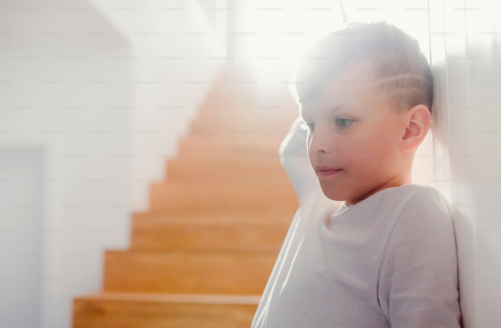A small boy standing indoors by the wooden stairs. Copy space.