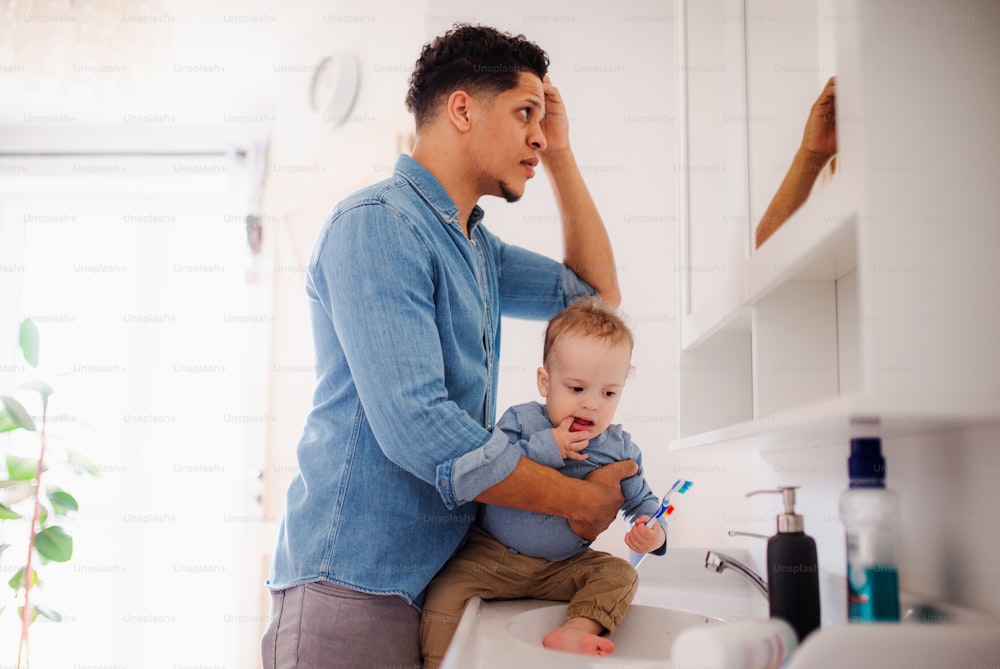 Padre joven e hijo pequeño en un baño en el interior de la casa, lavándose.