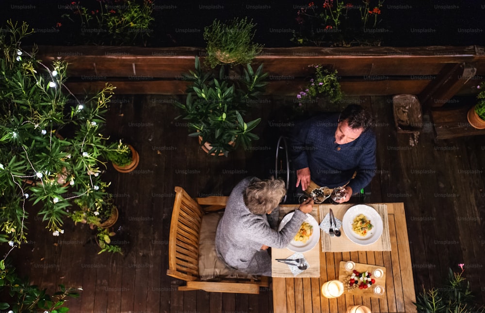 Top view of happy senior couple having dinner in the evening on terrace, drinking wine.