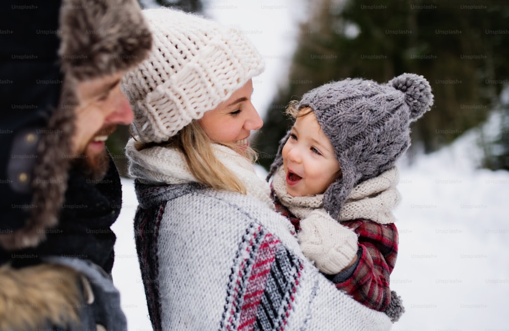 Vue latérale d’un père et d’une mère avec un petit enfant dans la nature hivernale, debout dans la neige.