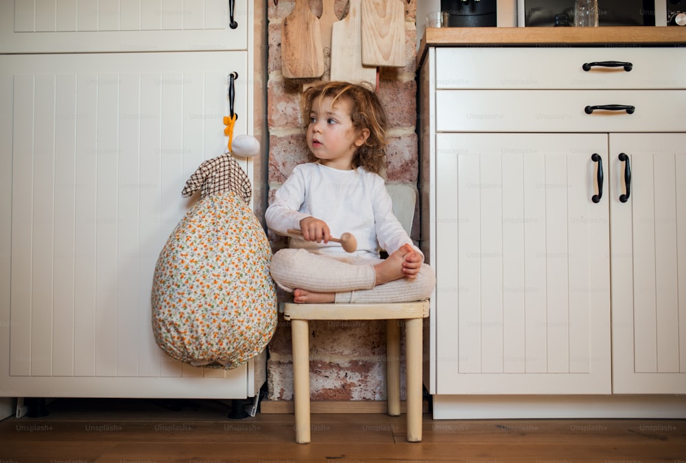 Retrato da vista frontal da menina do shopping sentada dentro de casa na cozinha em casa.