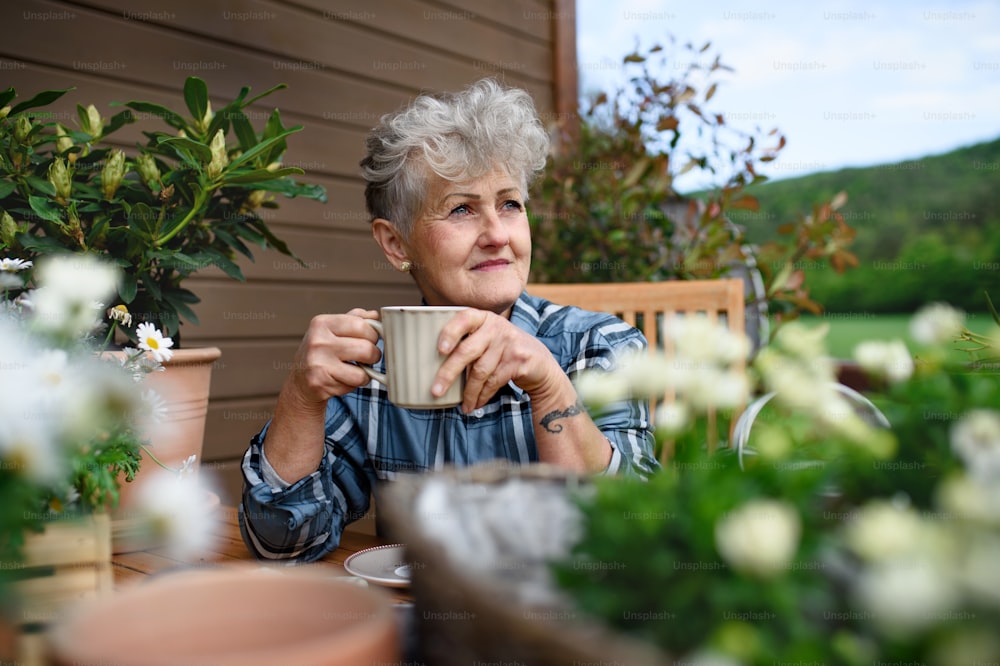 Portrait of senior woman with coffee sitting on terrace in summer, resting.