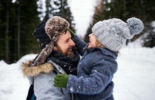 Vista lateral del padre con el hijo pequeño en la naturaleza nevada del invierno, hablando y riendo.