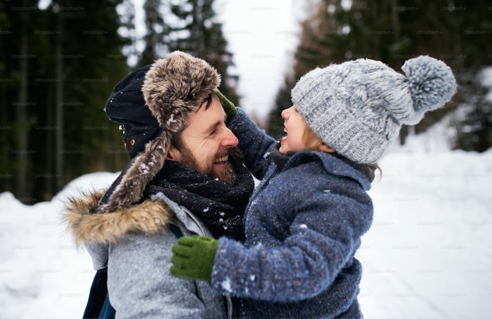 Side view of father with small son in snowy winter nature, talking and laughing.