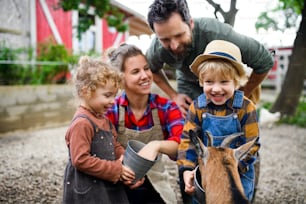 Portrait of happy family with small children standing on farm, feeding goat.
