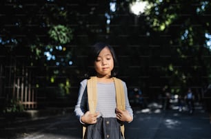 Retrato da vista frontal da menina japonesa pequena com mochila em pé ao ar livre na cidade.
