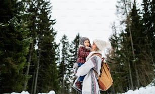 冬の自然の中に立つ小さな娘を連れた陽気な母親の横顔。
