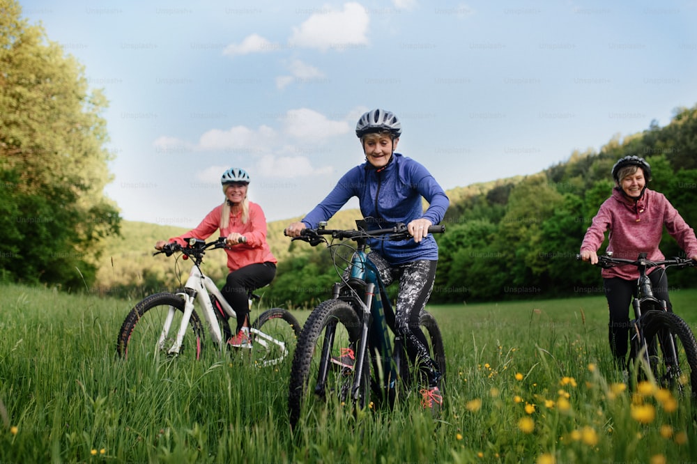 Happy active senior women friends cycling together outdoors in nature in meadow.