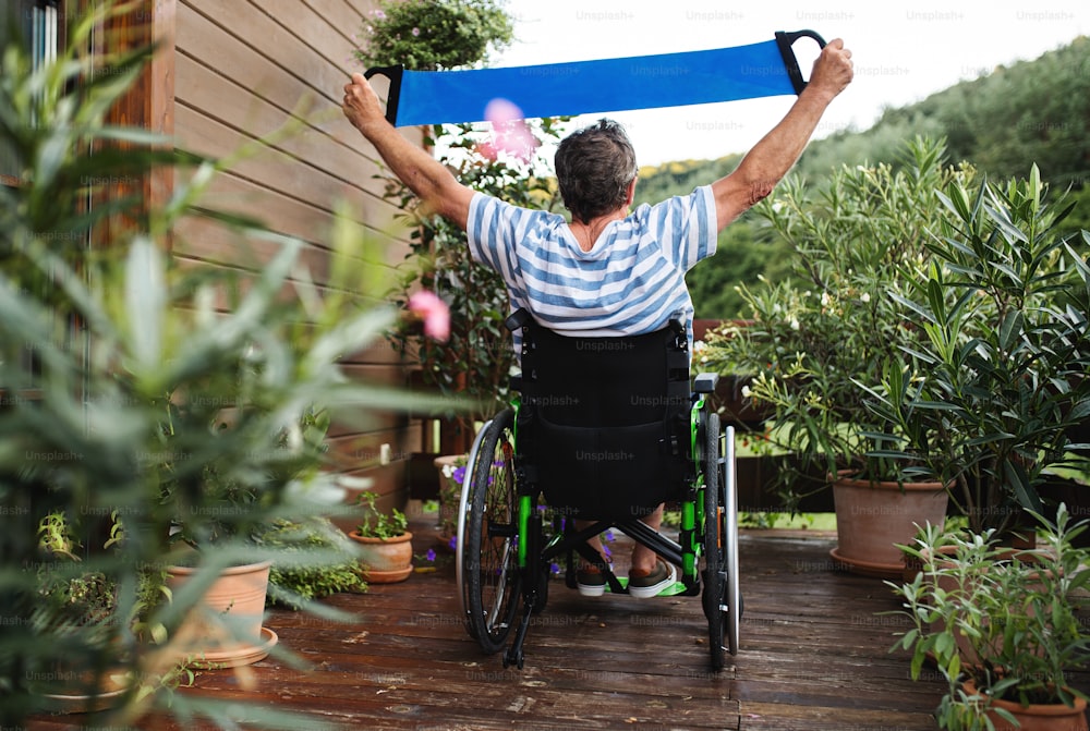 Eine Rückansicht eines älteren Mannes im Rollstuhl, der auf der Terrasse Sport treibt.