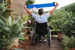 Vue arrière d’un homme âgé en fauteuil roulant faisant de l’exercice sur la terrasse.