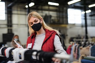 Woman volunteer working with clothes in community charity donations center, coronavirus concept.