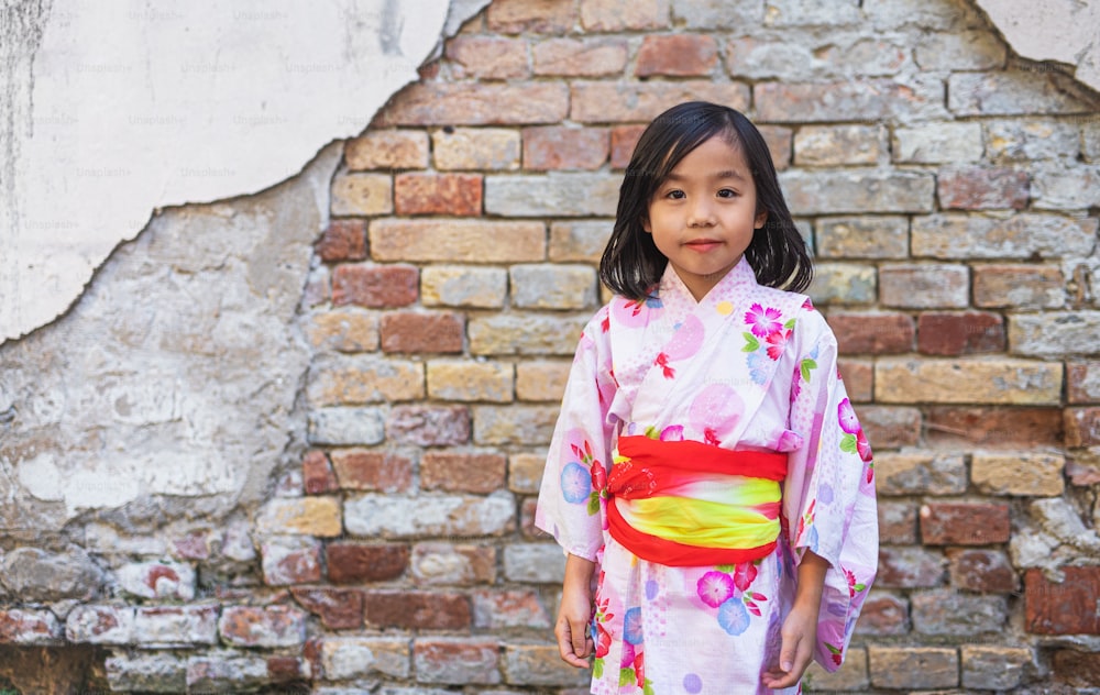 Porträt eines kleinen japanischen Mädchens, das im Freien in der Stadt einen Kimono trägt und in die Kamera schaut.