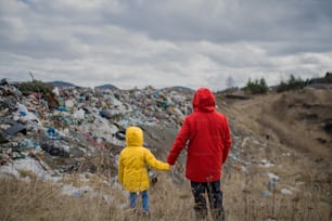 Rückansicht eines Mannes mit kleinem Kind, das auf der Mülldeponie steht und Händchen hält, Umweltkonzept.