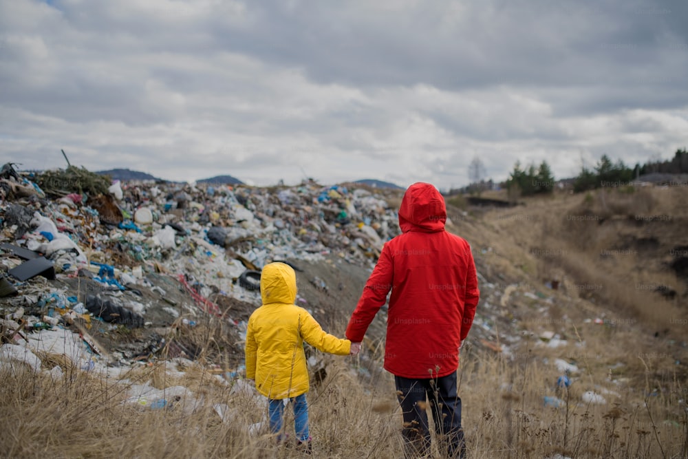 Rear view of man with small child standing and holding hands on landfill, environmental concept.