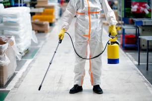 Front view portrait of man worker with protective mask and suit disinfecting industrial factory with spray gun.