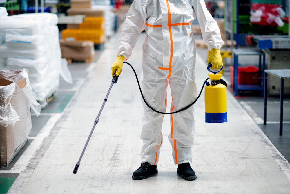 Vorderansicht Porträt eines Arbeiters mit Schutzmaske und Anzug desinfizierende Industriefabrik mit Spritzpistole.