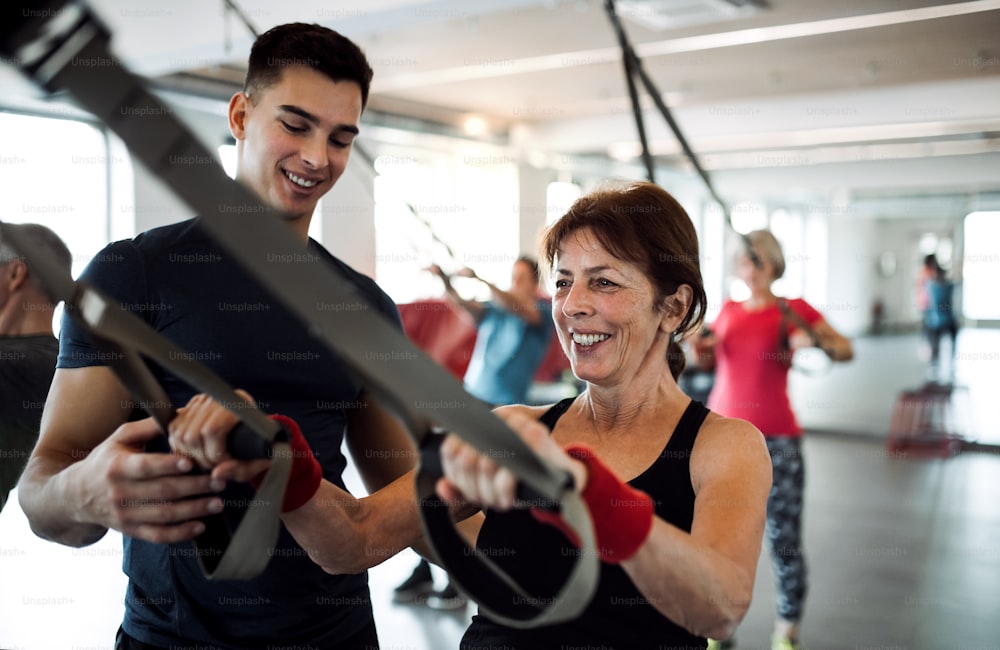 A group of cheerful seniors in gym with a young personal trainer doing exercise with TRX.