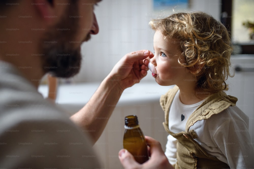 Père mûr méconnaissable donnant du sirop à sa petite fille malade à l’intérieur à la maison.