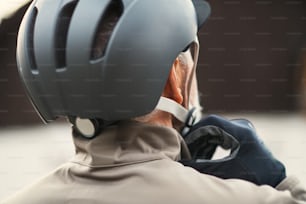 Una vista trasera de un hombre mayor activo parado al aire libre en la ciudad, poniéndose un casco de bicicleta. Un primer plano.