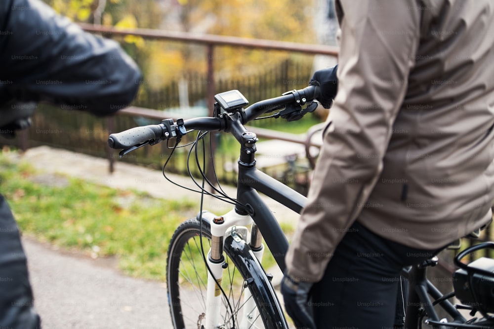 A midsection of active senior couple with helmets and electrobikes cycling outdoors on a road.