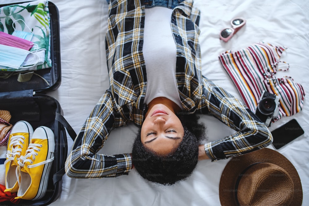 A top view of young woman with suitcase packing for holiday at home, coronavirus concept.