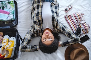 自宅での休日のためにスーツケースを梱包した若い女性、コロナウイルスのコンセプトの上から見た図。