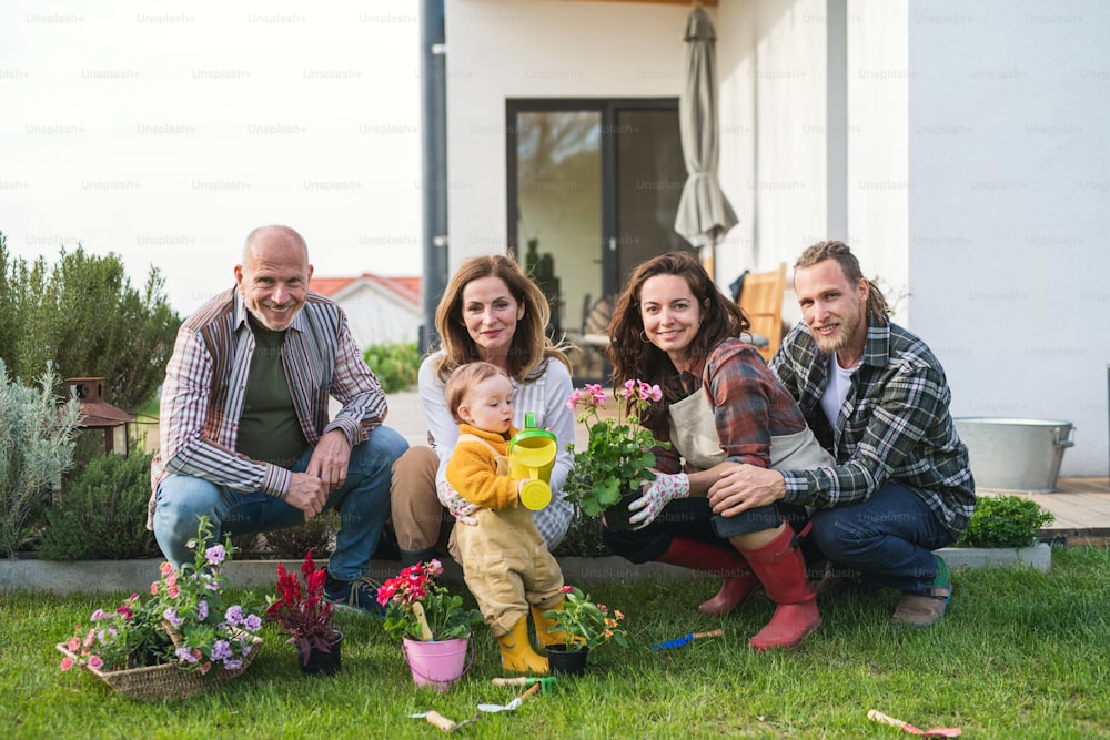 Una familia multigeneracional feliz al aire libre plantando flores en el jardín de la casa, concepto de jardinería.