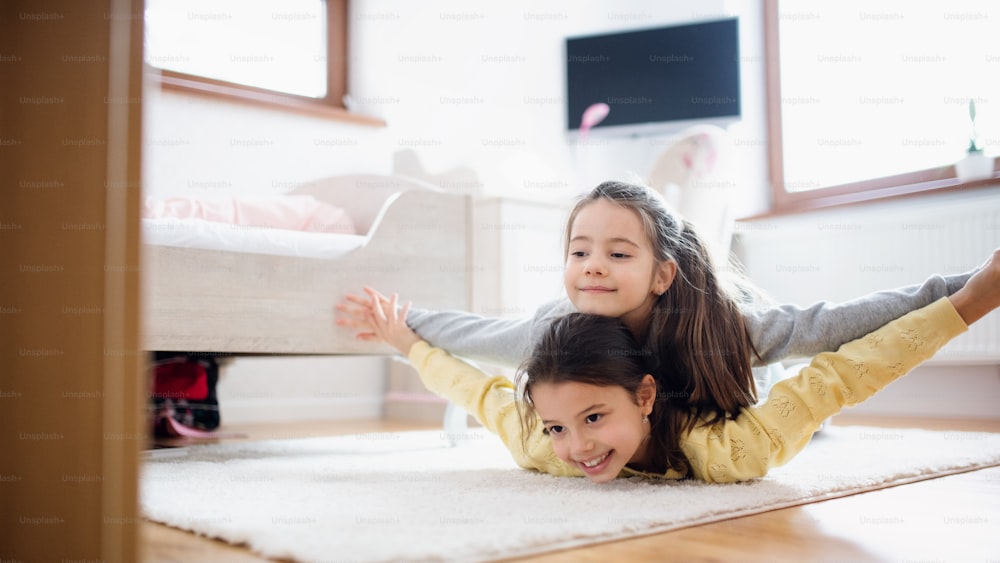 두 명의 어린 소녀 자매가 집 실내에서 침실 바닥에서 놀고 있습니다.