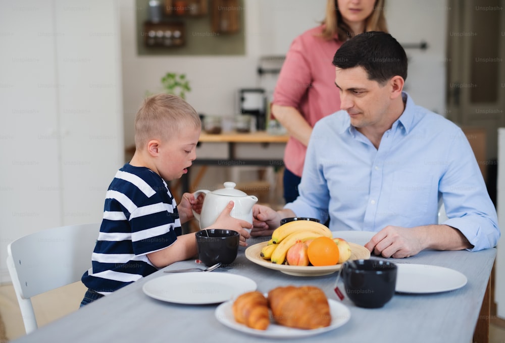 Una familia feliz con un hijo con síndrome de down en la mesa, desayunando.