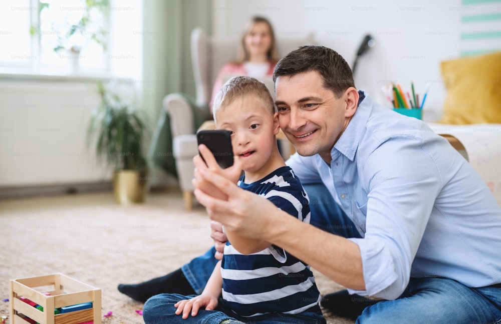 Padre feliz con un hijo feliz con síndrome de down en el interior de la casa, tomando selfies con el teléfono inteligente.