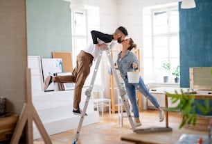 Happy mid adults couple kissing when painting indoors at home, relocation and diy concept.