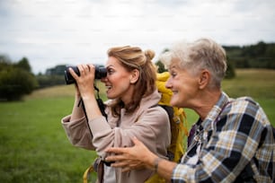 A happy senior mother hiker with adult daughter looking through binoculars outdoors in nature