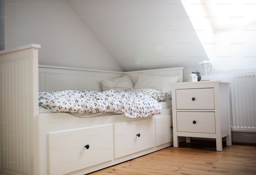 White wooden single bed wnd bedside table indoors in bedroom at home.