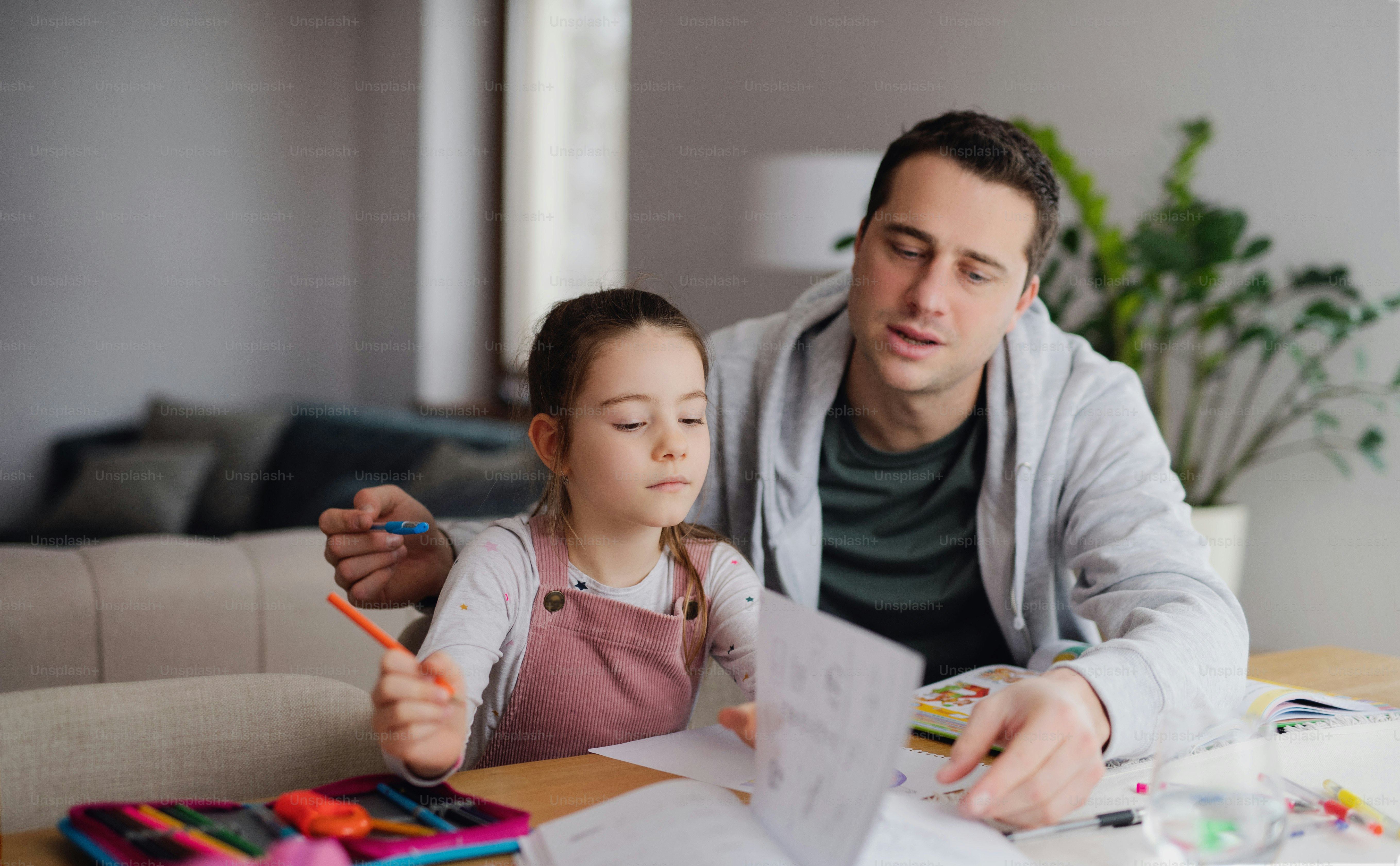 Father helping small daugther with homework indoors at home, distance learning.