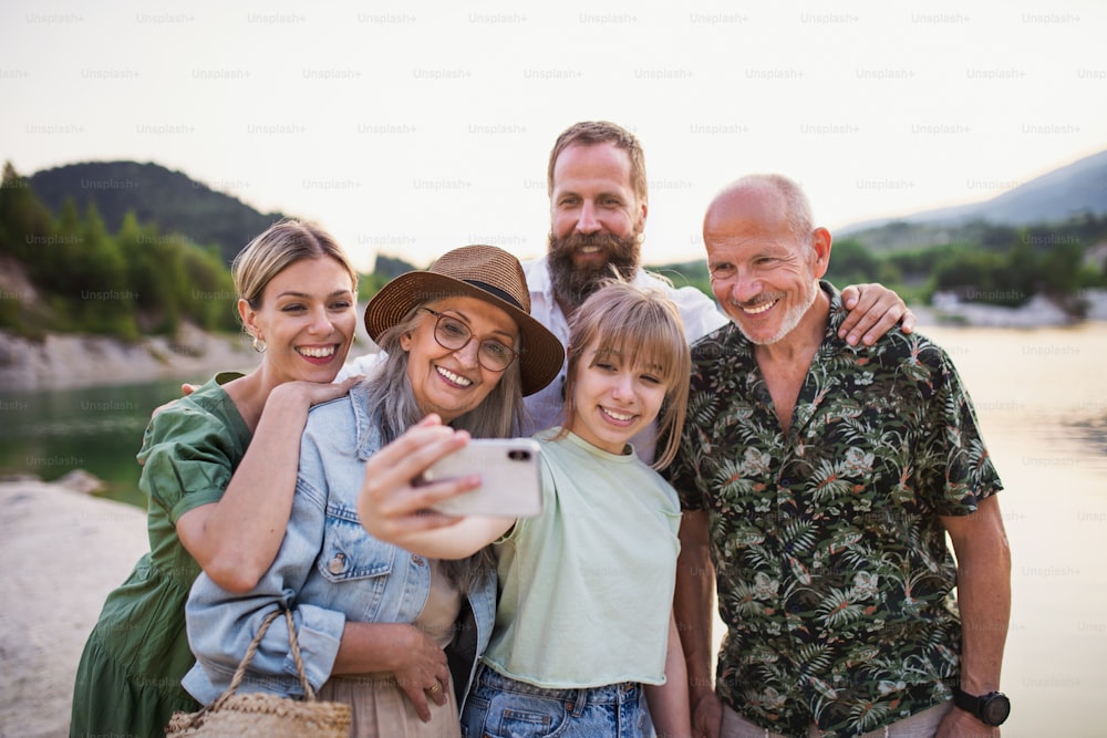 Une famille multigénérationnelle heureuse en randonnée pendant les vacances d’été, en prenant un selfie.