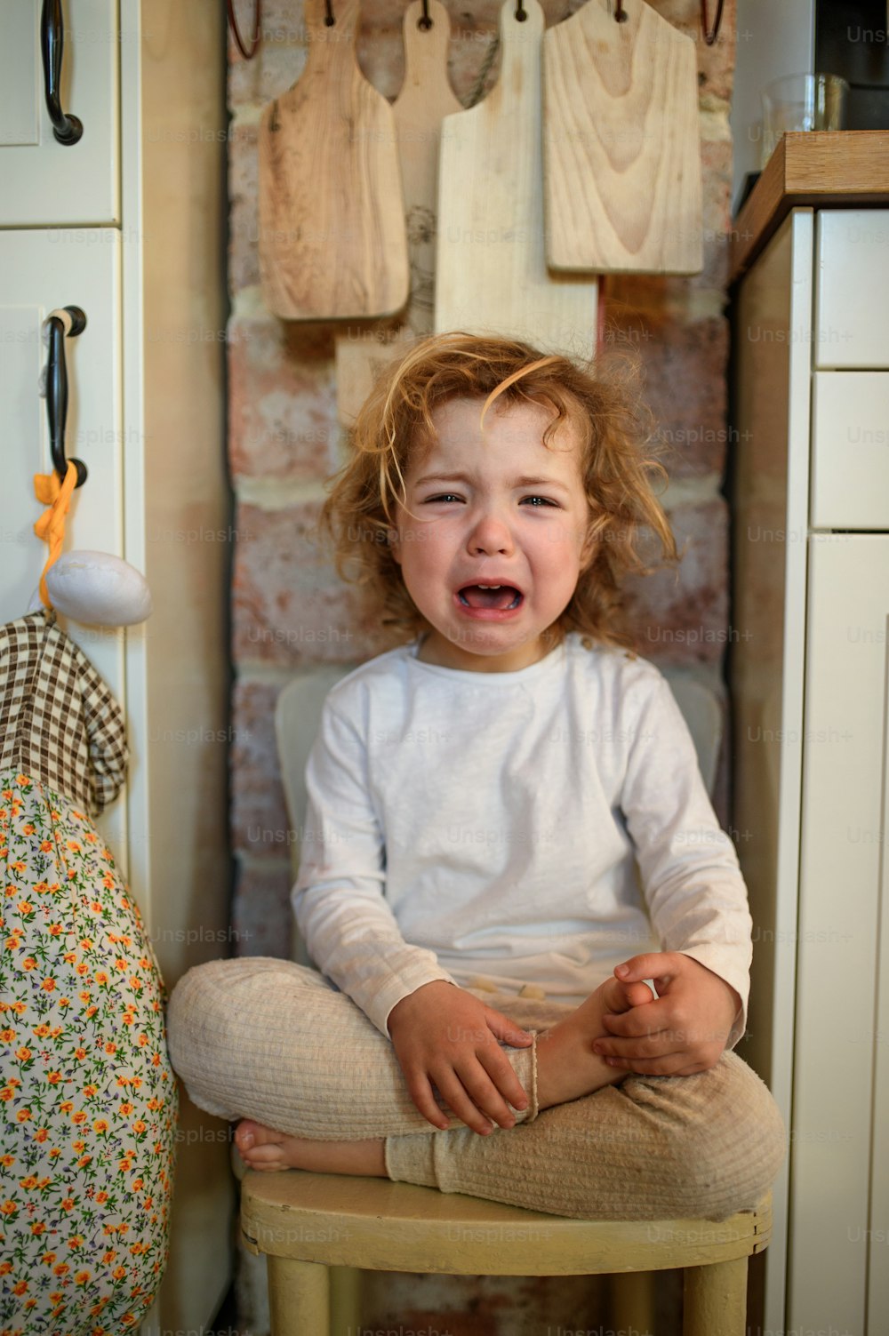 Porträt eines unglücklichen kleinen Mädchens, das zu Hause drinnen in der Küche sitzt, in die Kamera schaut und weint.
