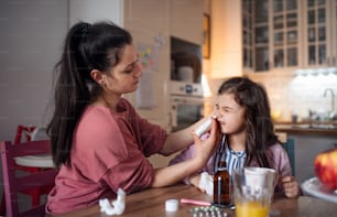 Portrait of mother looking after sick small daughter at home, using nasal spray.
