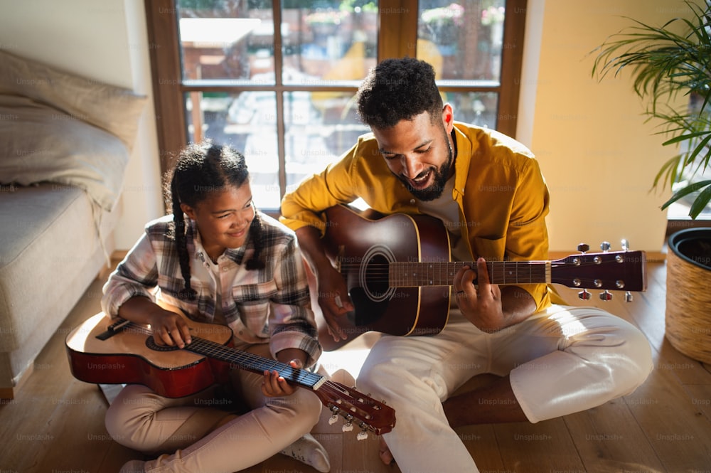 A high-angle view of happy father with small daughter indoors at home, playing guitar.