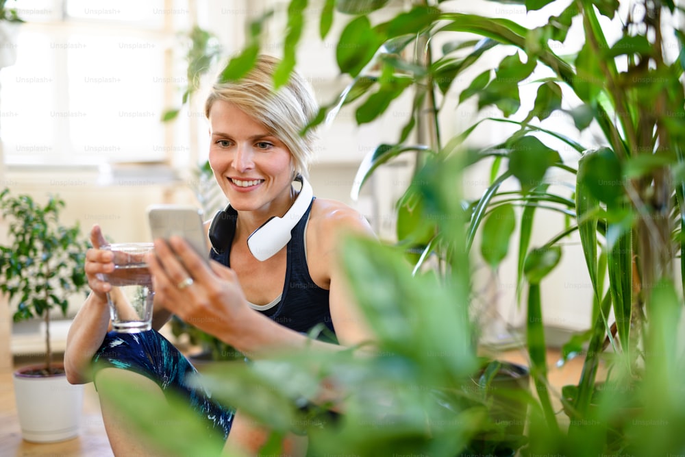 Front view of young sports woman with smartphone indoors at home, resting. Copy space.