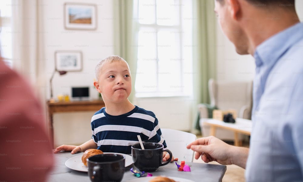 A portrait of down syndrome boy with parents at the table, having breakfast.