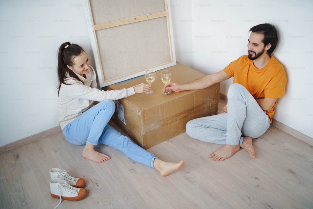 Feliz pareja joven con cajas y vino que se muda en un nuevo piso, un nuevo hogar y un concepto de reubicación.