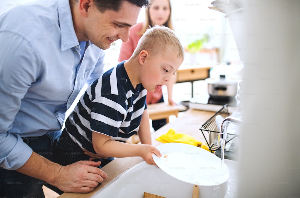 A father with down syndrome son indoors in kitchen, washing dishes.