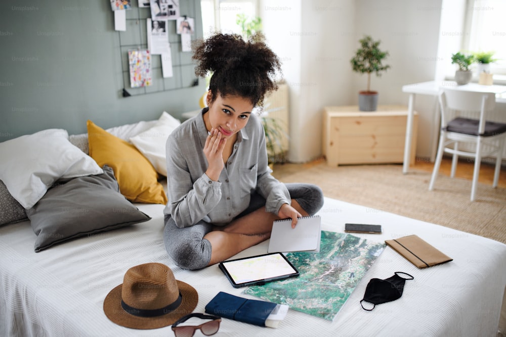 Mulher jovem feliz com tablet e mapa dentro de casa em casa, planejando a viagem de viagem.