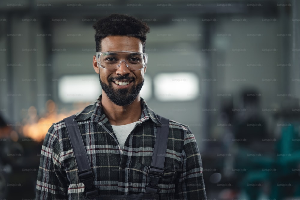 A portrait of young industrial man working indoors in metal workshop, looking at camera.