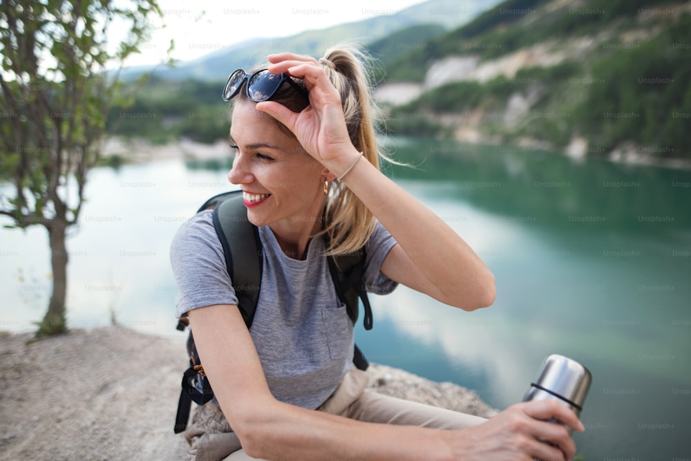 A mid adult woman tourist on hiking trip on summer holiday, resting by lake.