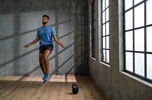 A young African American sportsman using jumping rope indoors, workout training concept.