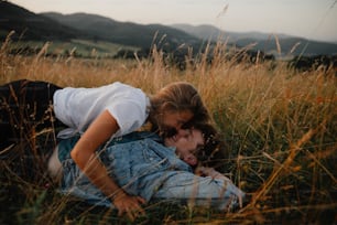 A young couple on a walk in nature in countryside, lying in grass laughing.