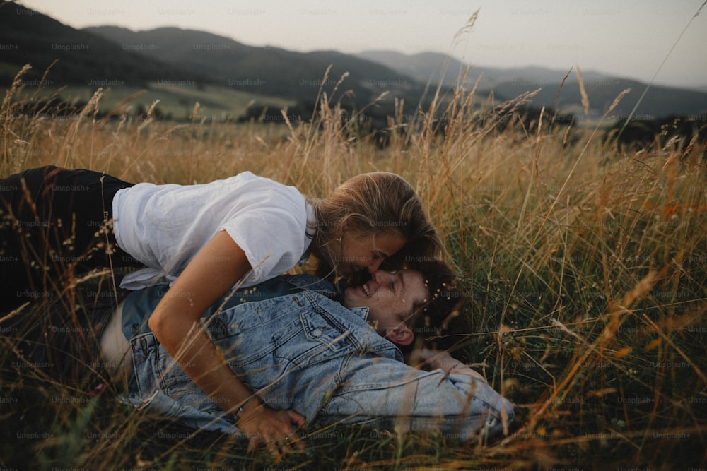 A young couple on a walk in nature in countryside, lying in grass laughing.