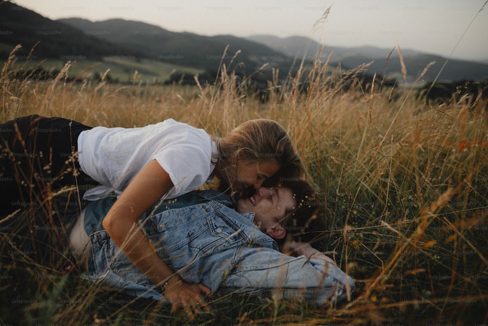 Una pareja joven en un paseo por la naturaleza en el campo, tumbado en la hierba riendo.